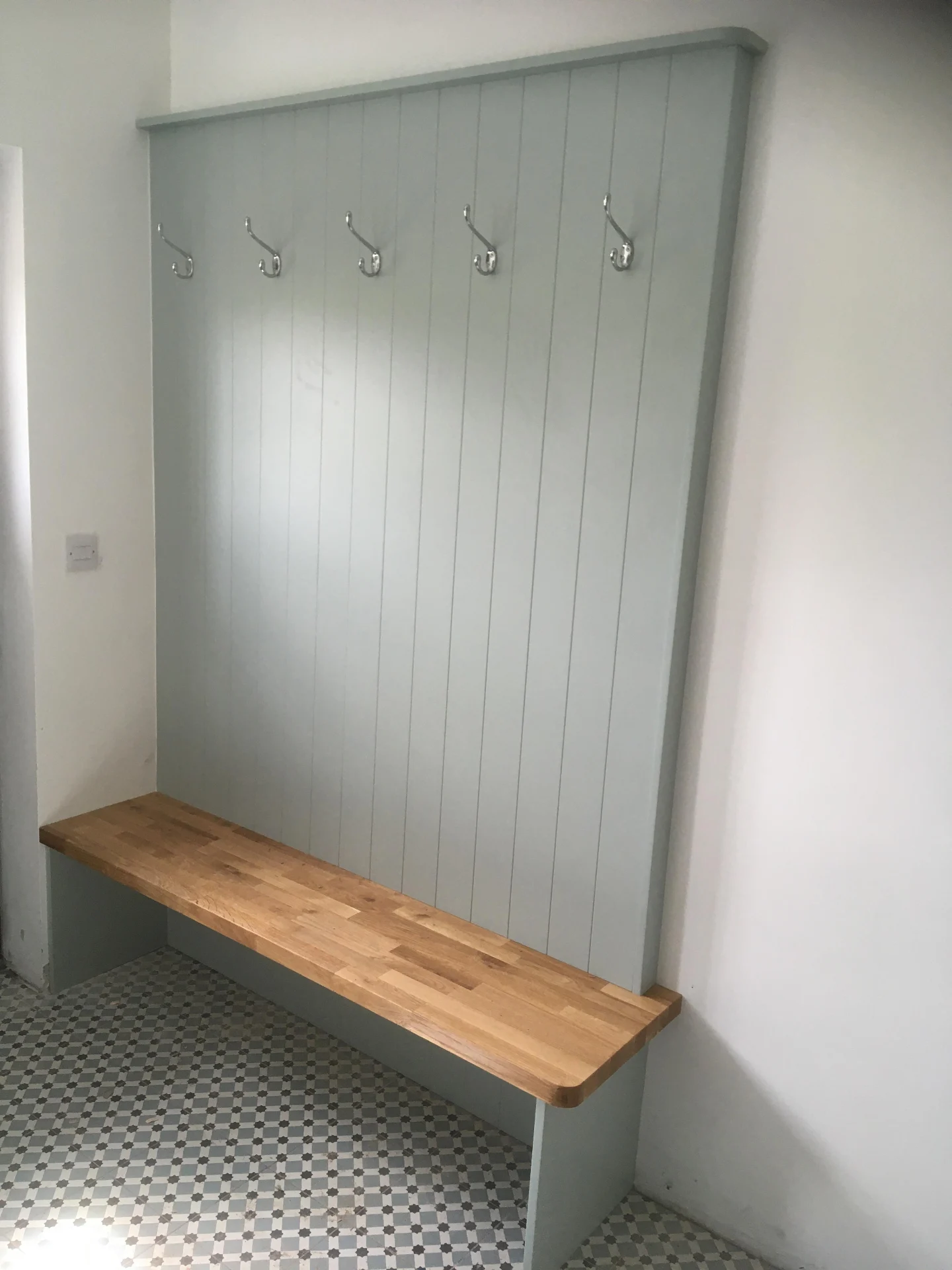 Grey boot room storage with fitted bench, hooks and overhead shelving.