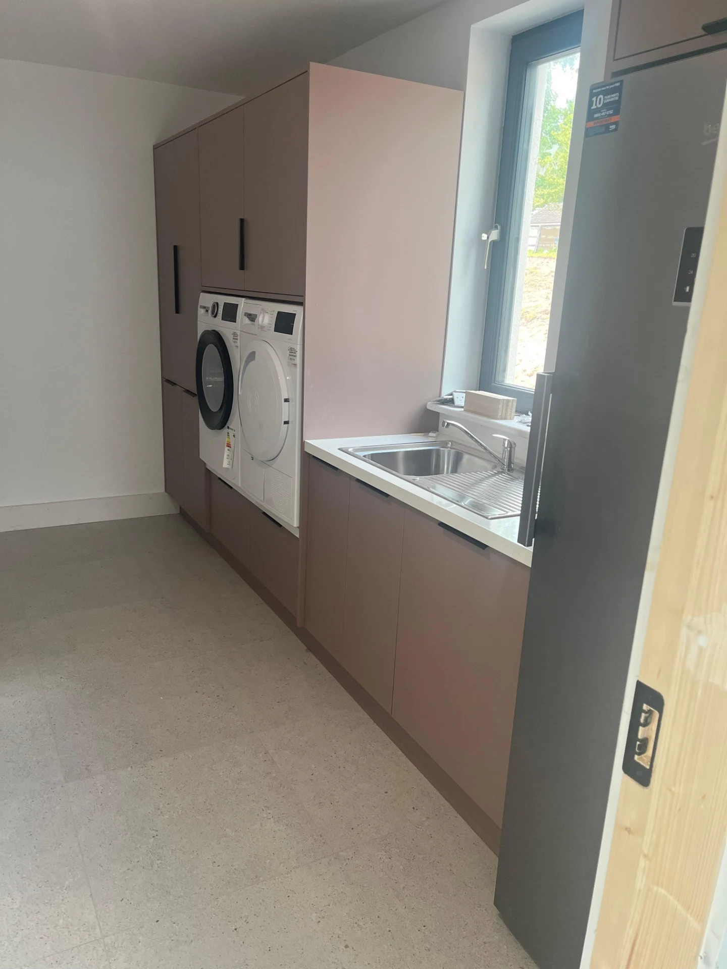 Pink utility laundry room with fitted cabinetry and appliance storage.