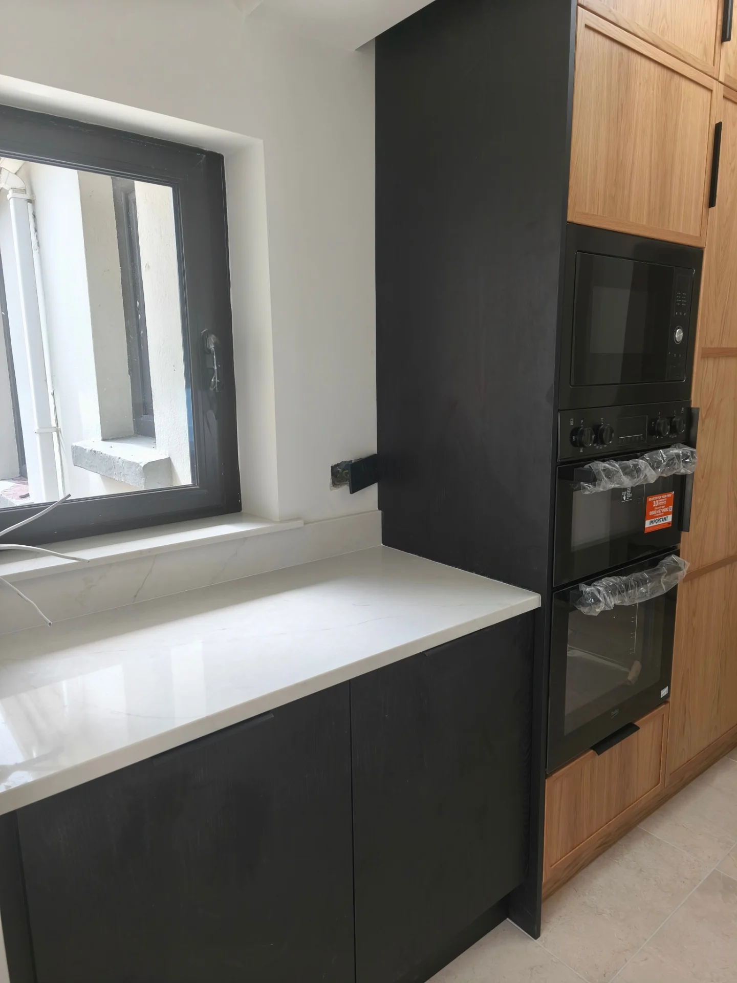 Black and oak kitchen appliance wall with tall fitted cabinetry and integrated ovens.