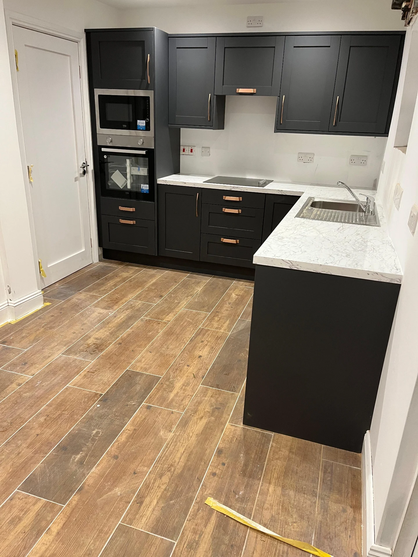 Compact charcoal fitted kitchen with copper handles and warm worktop detail.