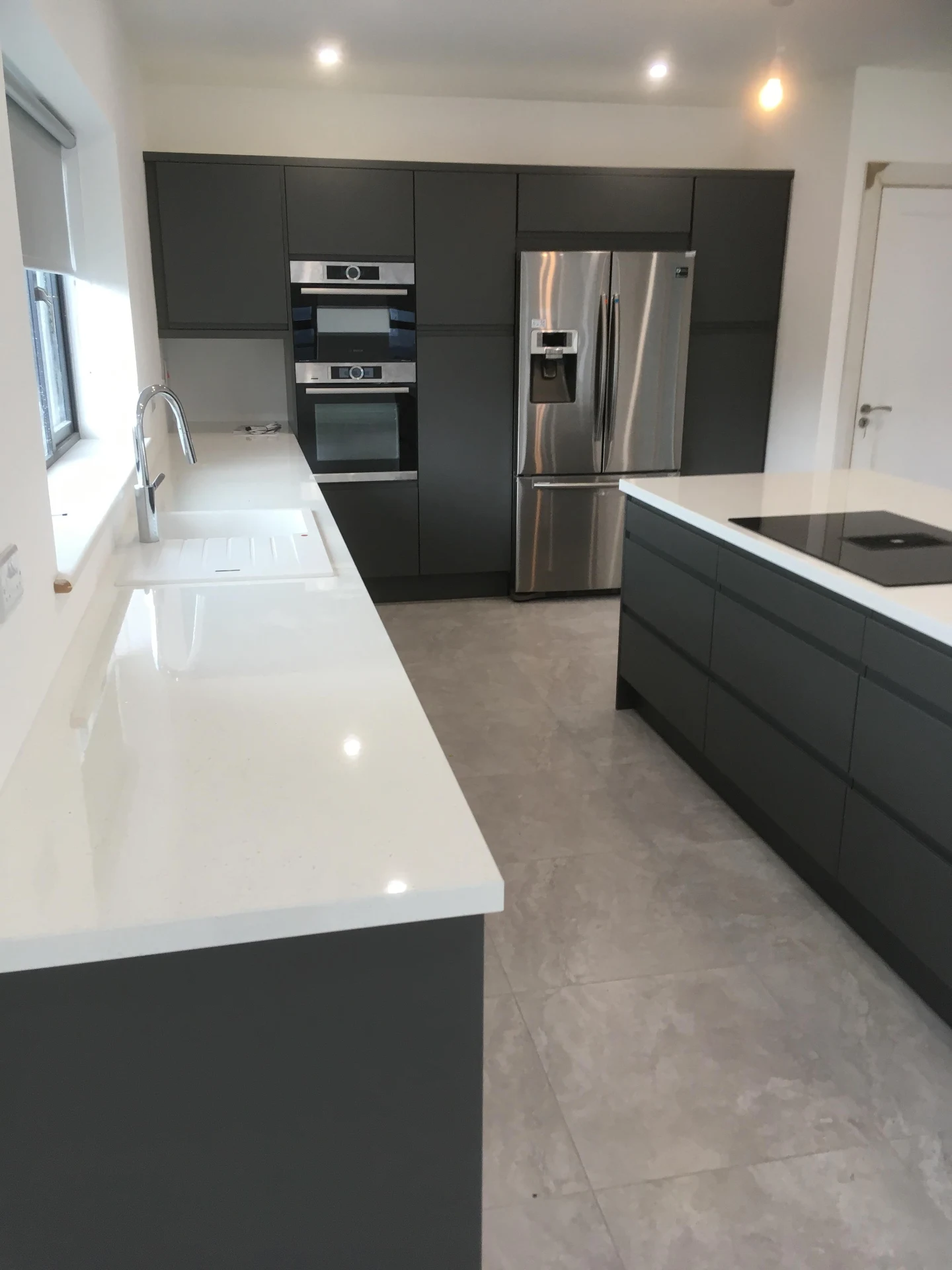 Charcoal fitted kitchen with island, tall storage and warm timber detailing.