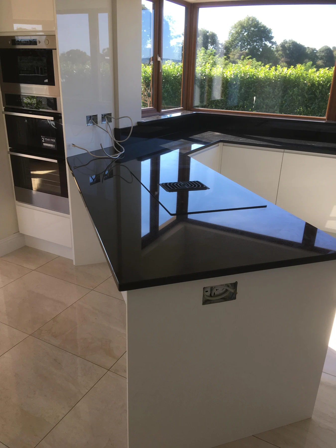 White kitchen island with black worktop, fitted drawers and pendant lighting.