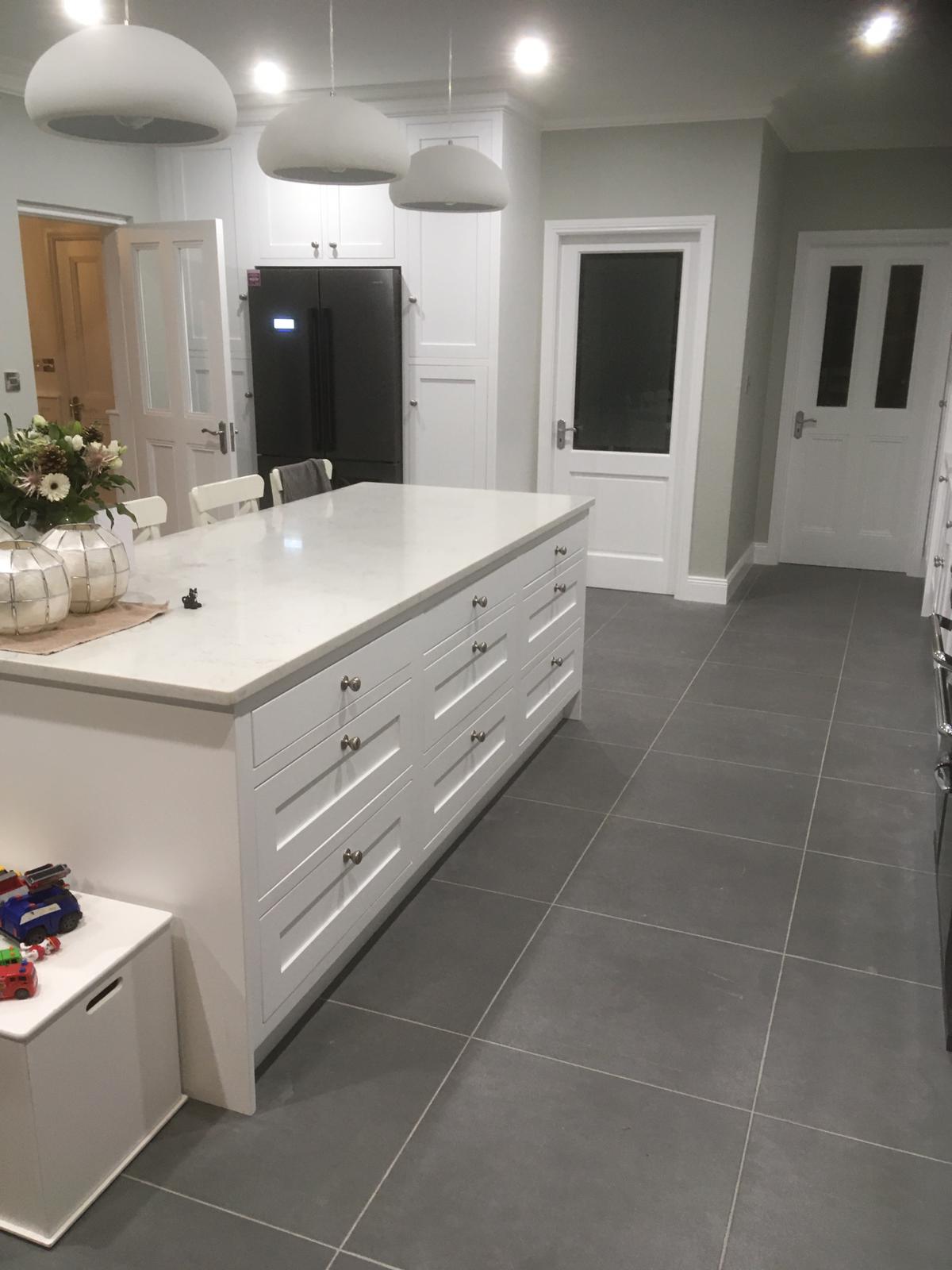 White fitted kitchen with island, tall storage and a black fridge.