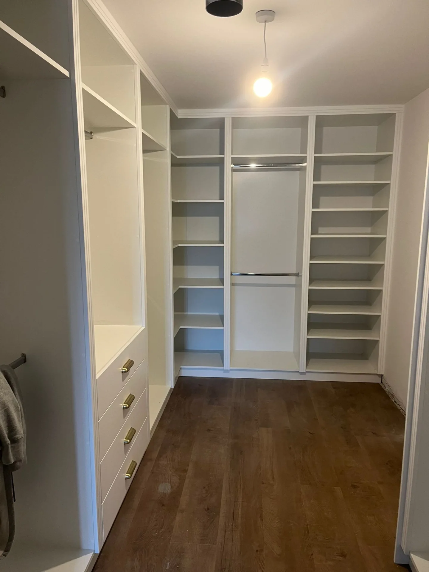 Walk-in wardrobe interior with white open shelving, hanging space and drawer storage.